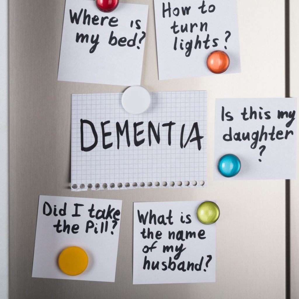 Close-up of dementia notes with various reminders attached with magnetic thumbtacks on a refrigerator.