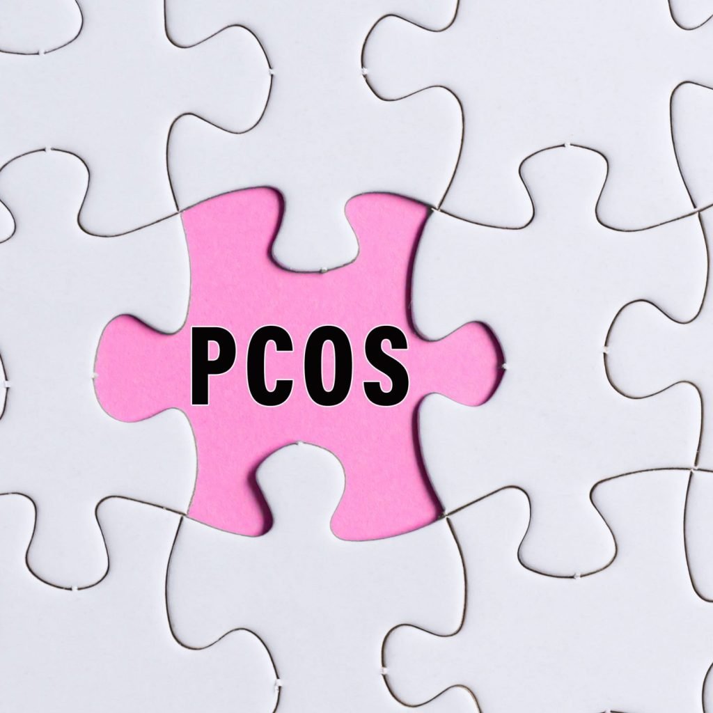 polycystic ovary syndrome (PCOS) text on white jigsaw puzzle over pink background.