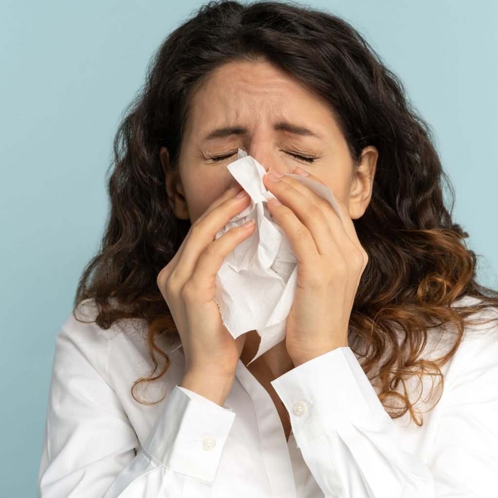 A woman sneezing into a paper tissue.
