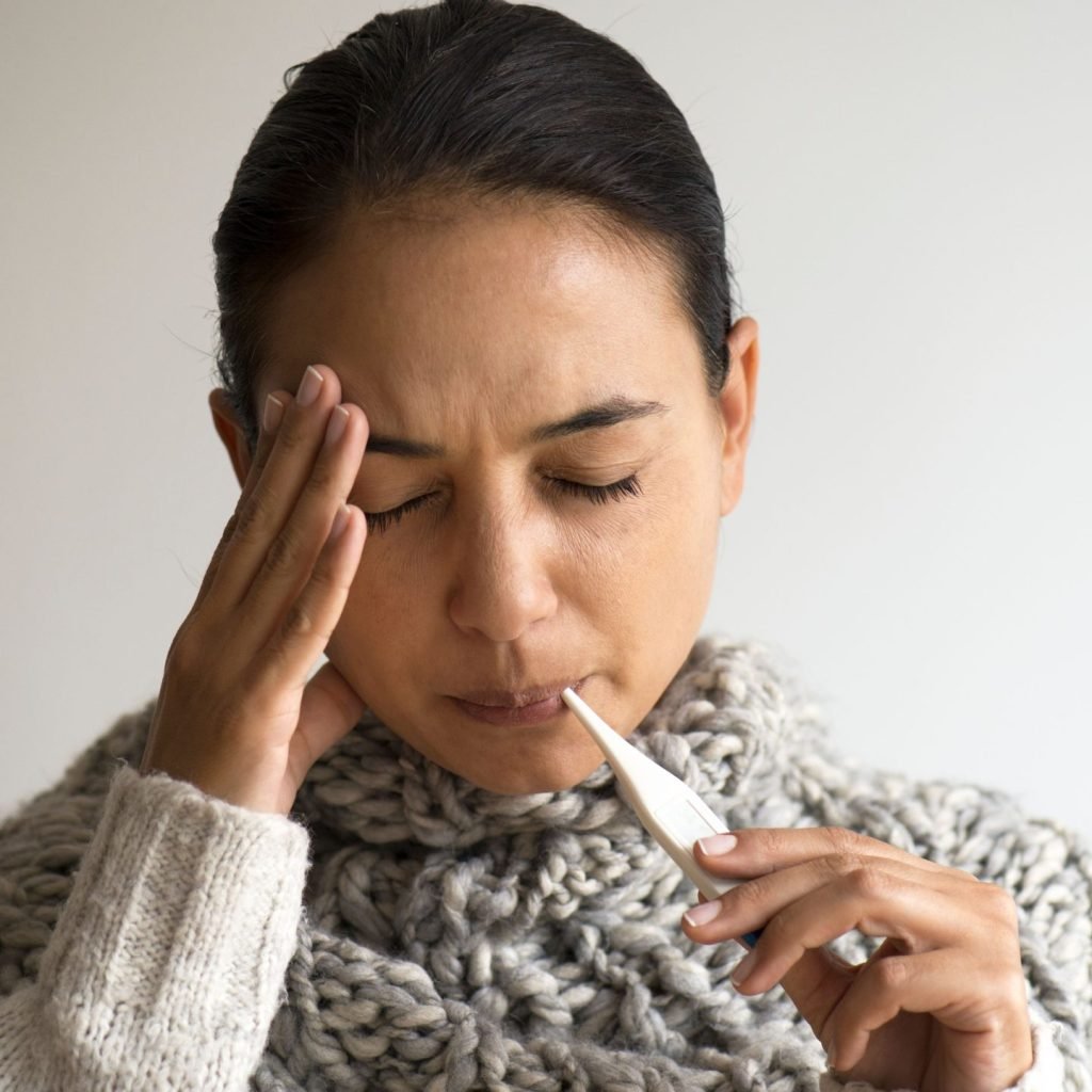 A young woman is seen to be suffering from fever and using a thermometer to know her body temperature.