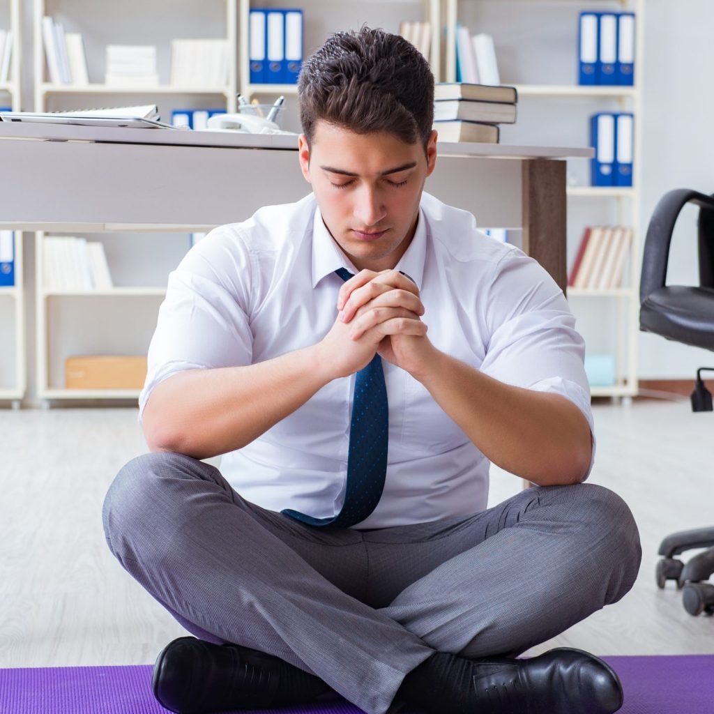 A concept image of Workplace Wellness: a man in a zen poise during a work break relaxing.
